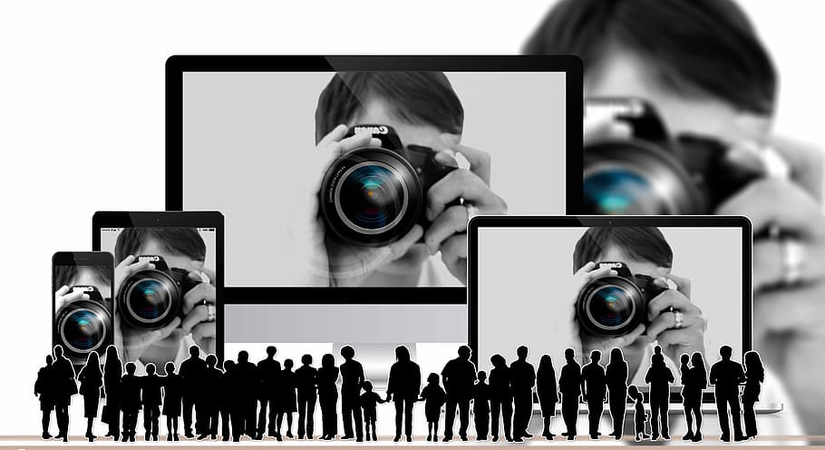 Several large screens shows a man taking a photo, with a large group of small individual silhouettes at the front