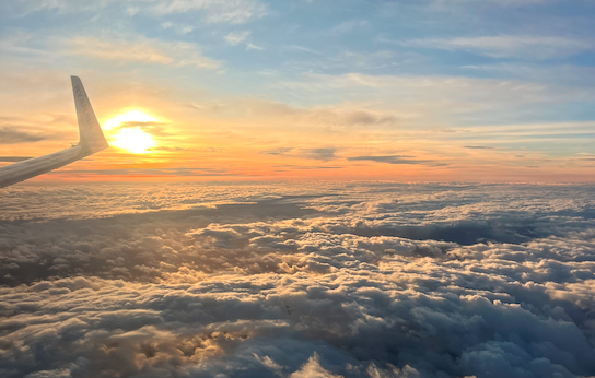 View of the sun setting above the clouds, lighting up the sky with an orange glow, with an aeroplane wing tip on the left